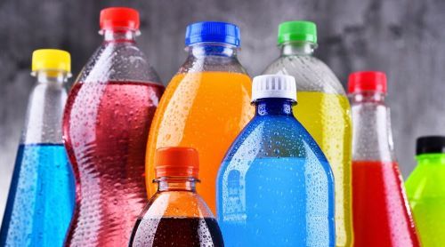The photo shows plastic bottles filled with coloured liquids representing sweet soft drinks.